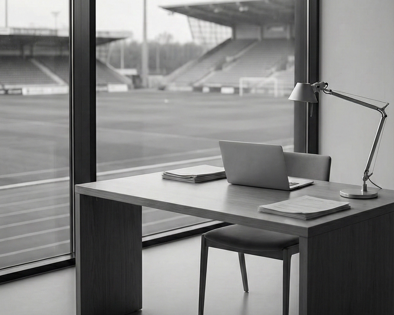 Escritorio de oficina con ventana que da a un estadio deportivo, en una fotografía en blanco y negro